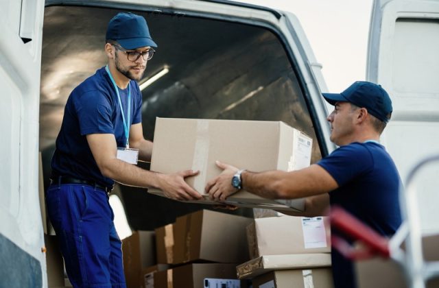 Delivery men loading carboard boxes in a van while getting ready for the shipment.